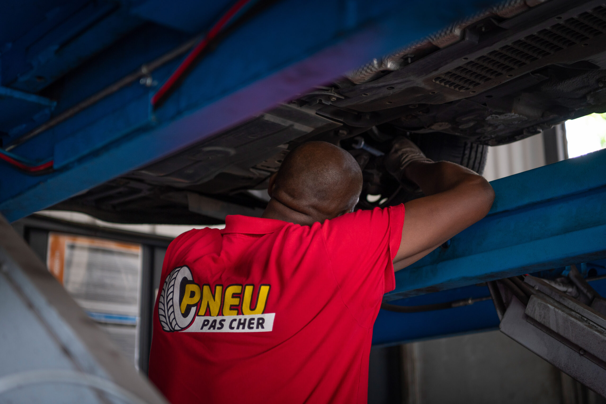 Mécanicien Pneu Pas Cher effectuant le réglage du parallélisme sous une voiture sur un pont élévateur au centre de Schoelcher